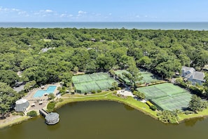 Ein Tennisplatzkomplex, umgeben von üppigem Grün, einem Schwimmbad und einem kleinen See.