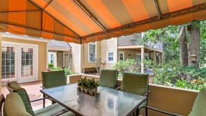 Un patio exterior con una mesa y sillas de vidrio, rodeado por un toldo a rayas.