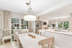 A modern kitchen with a central island, white cabinetry, and a dining area with a table and chairs.