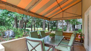 Un patio exterior con una mesa y sillas, rodeado por una zona cubierta con un toldo a rayas.