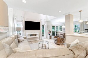 A modern living room with a beige sofa, a flat-screen TV, and a glass coffee table.