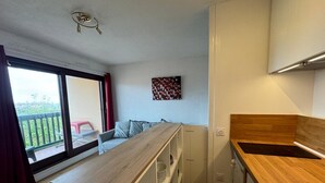 Een compacte keuken met een houten aanrecht, een zithoek met een rode stoel, en een balkon met uitzicht.