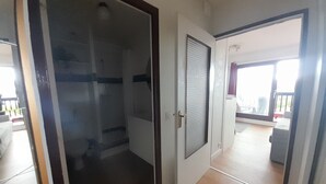 Een gang met een glazen deur die uitkomt in een kamer met betegelde vloer.