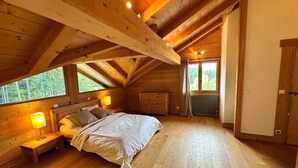Un dormitorio rústico de cabaña de madera con cama, lámparas de noche y ventana con vistas a un bosque.