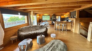 Interior acogedor de una cabaña con comedor, cocina y grandes ventanas que ofrecen vistas al verdor.