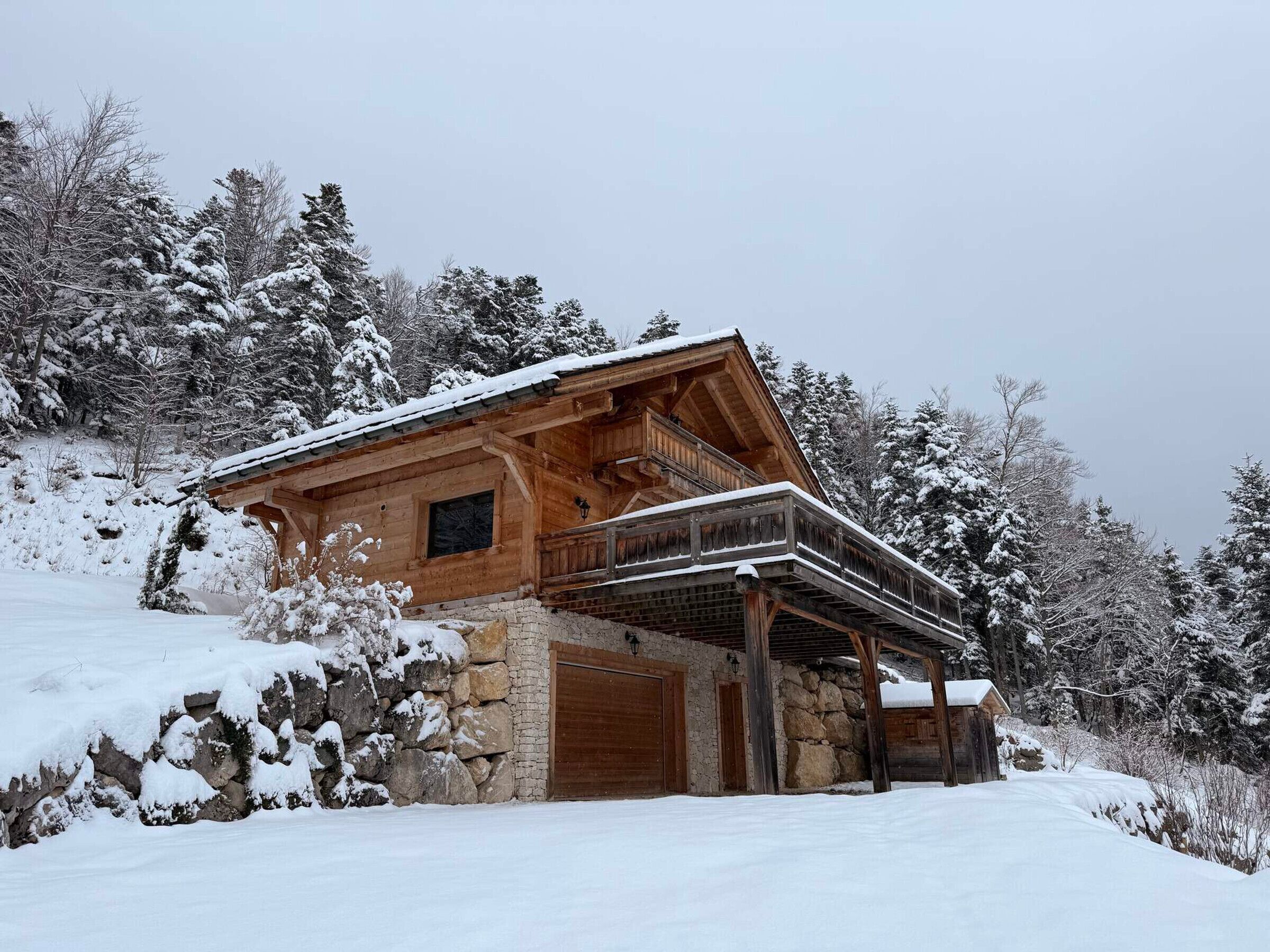 Een houten chalet met een stenen fundering, een balkon en een besneeerd landschap.