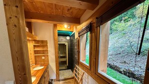 Interior de madera con lavamanos de madera, ducha y ventana con vistas a un bosque.