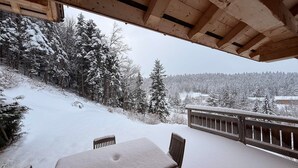 Una terraza cubierta de nieve con una mesa y sillas, con vistas a un paisaje nevado con árboles y edificios.
