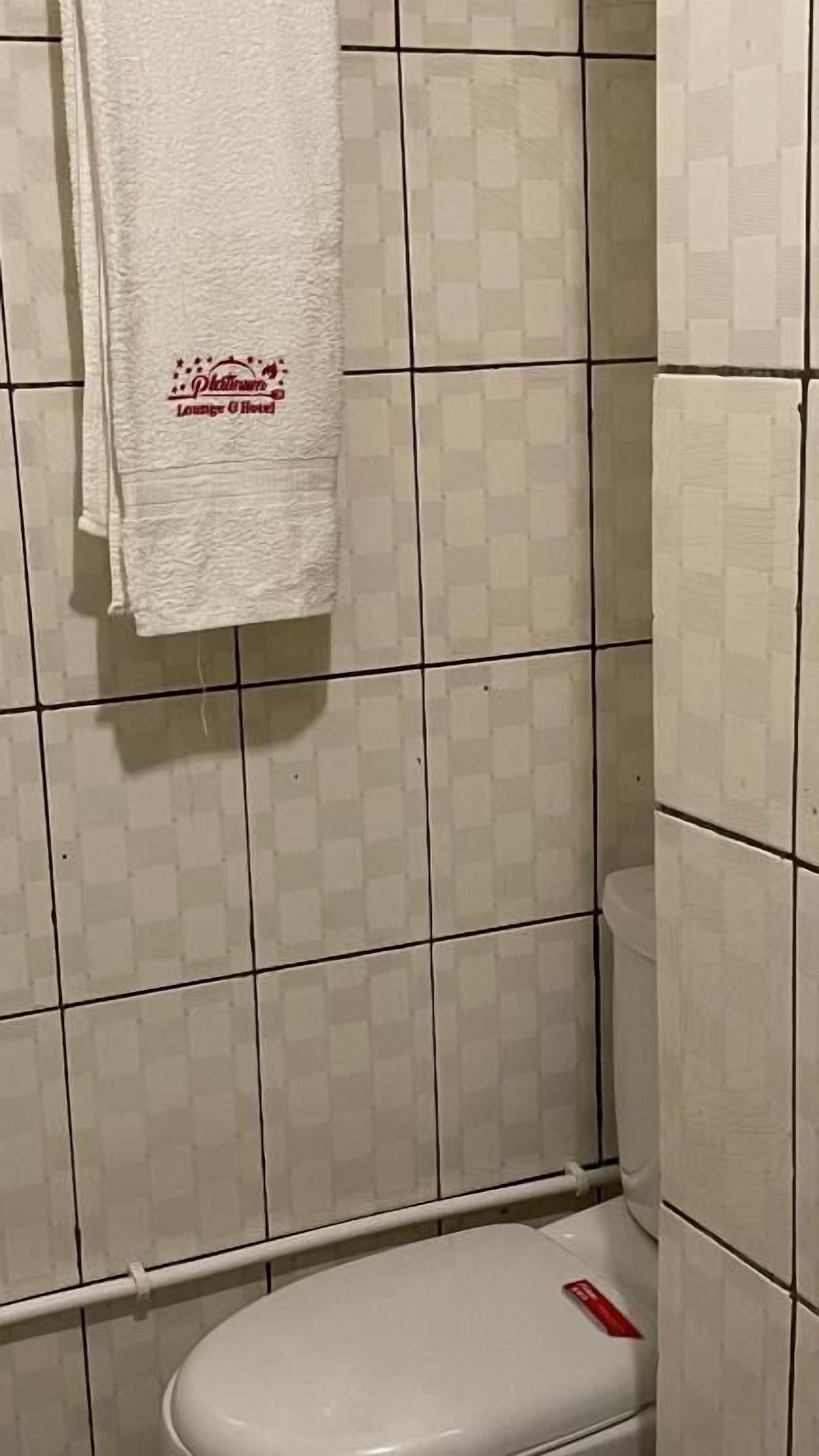 Un baño con pared de azulejos blancos, un inodoro blanco y una toalla blanca colgada en la pared.