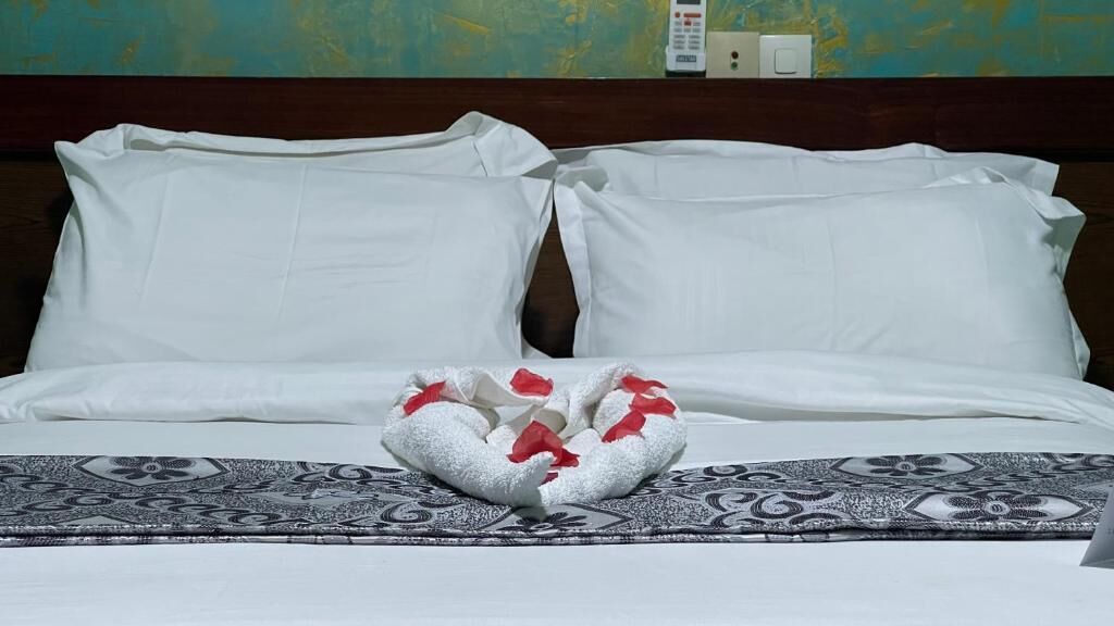 Un lit bien fait, avec du linge de lit blanc et une serviette décorative ornée de rubans rouges.