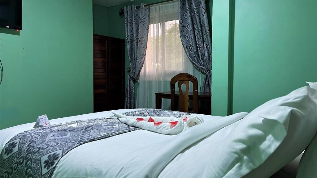 A room with a bed, a wooden chair, and a window with curtains.