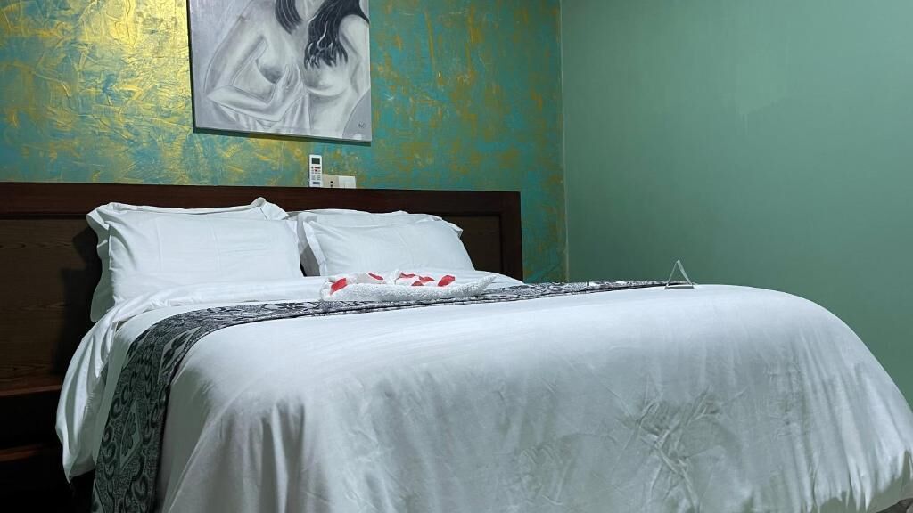 Un letto rifatto con lenzuola bianche e una coperta decorata, un quadro appeso al muro e una testiera in legno.