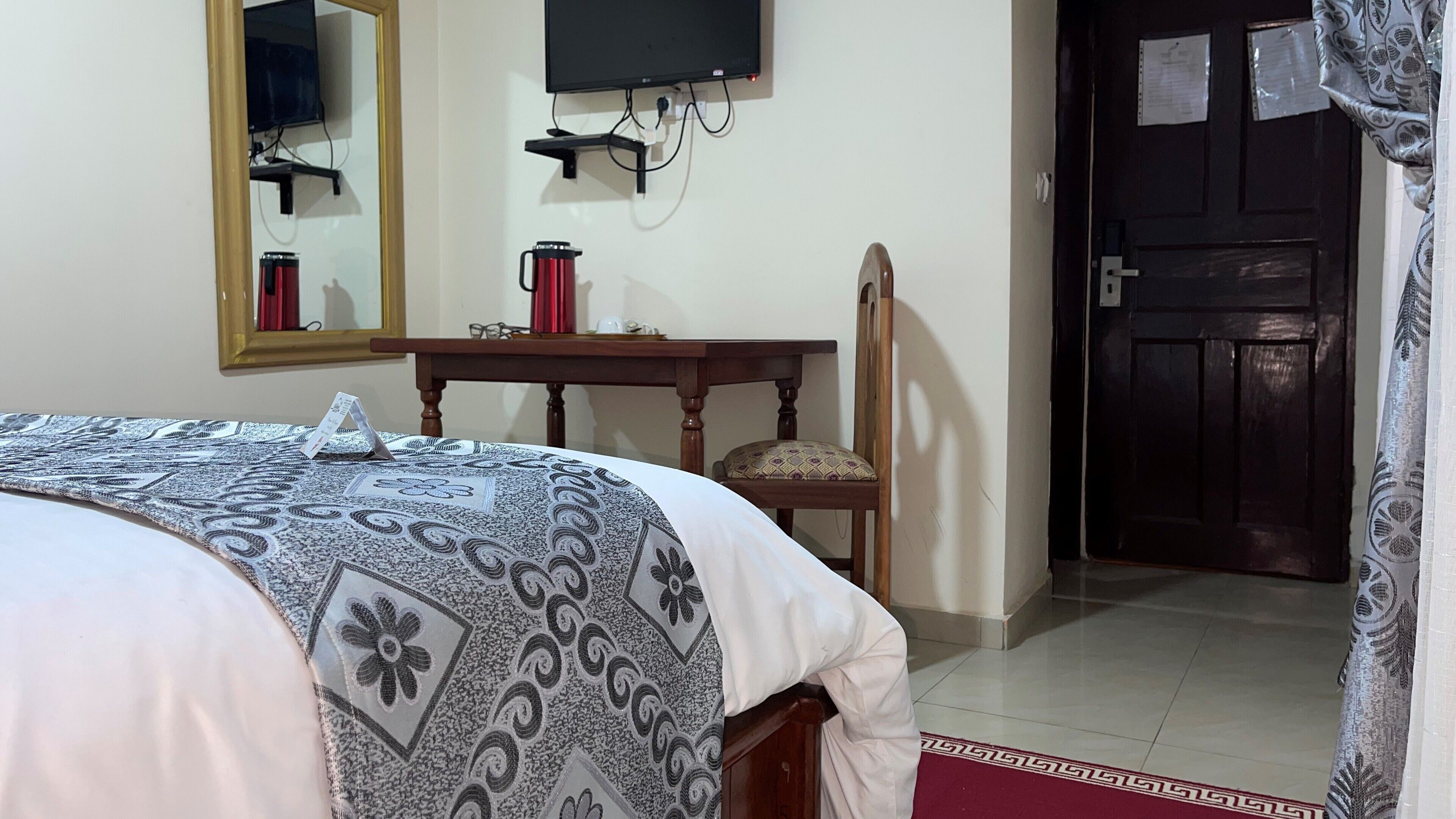 A hotel room with a bed, a wooden nightstand, a chair, a television mounted on the wall, and a door.