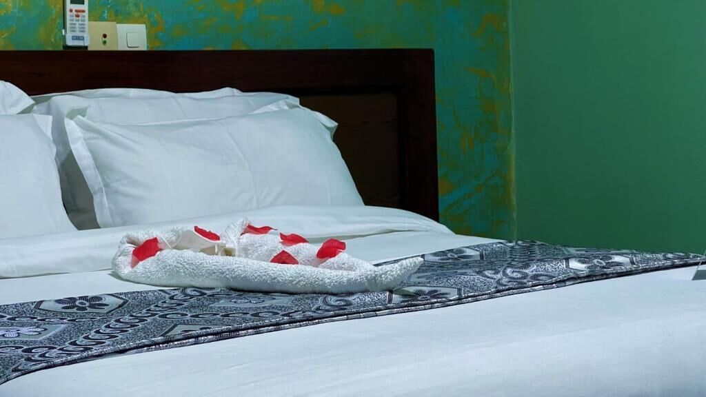 A neatly made bed with white linens and a decorative towel with red flowers.