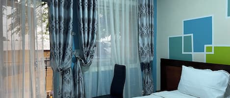 A hotel room with a bed, a chair, and curtains.