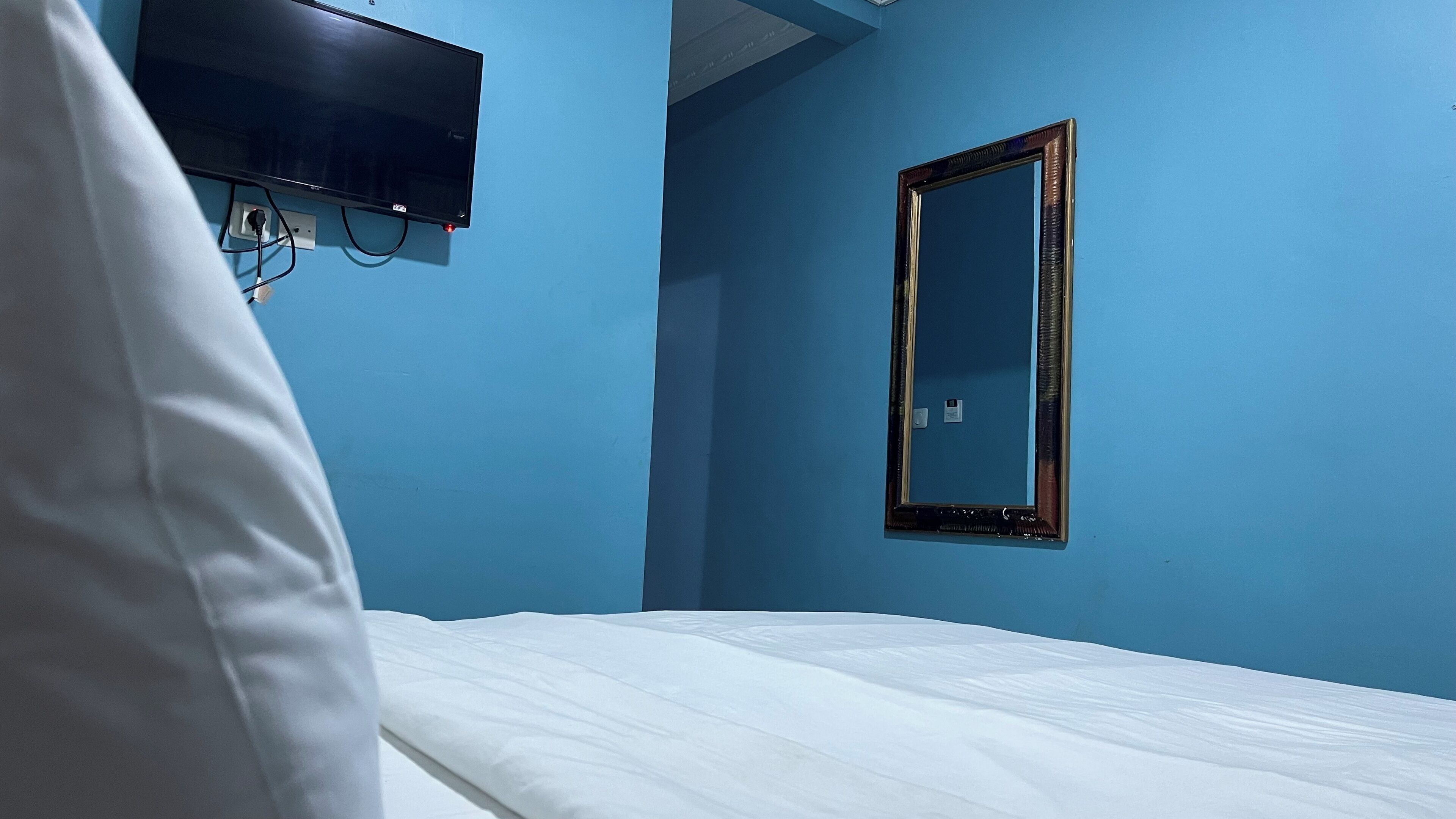 Una habitación con una cama, un televisor montado en la pared y un espejo.