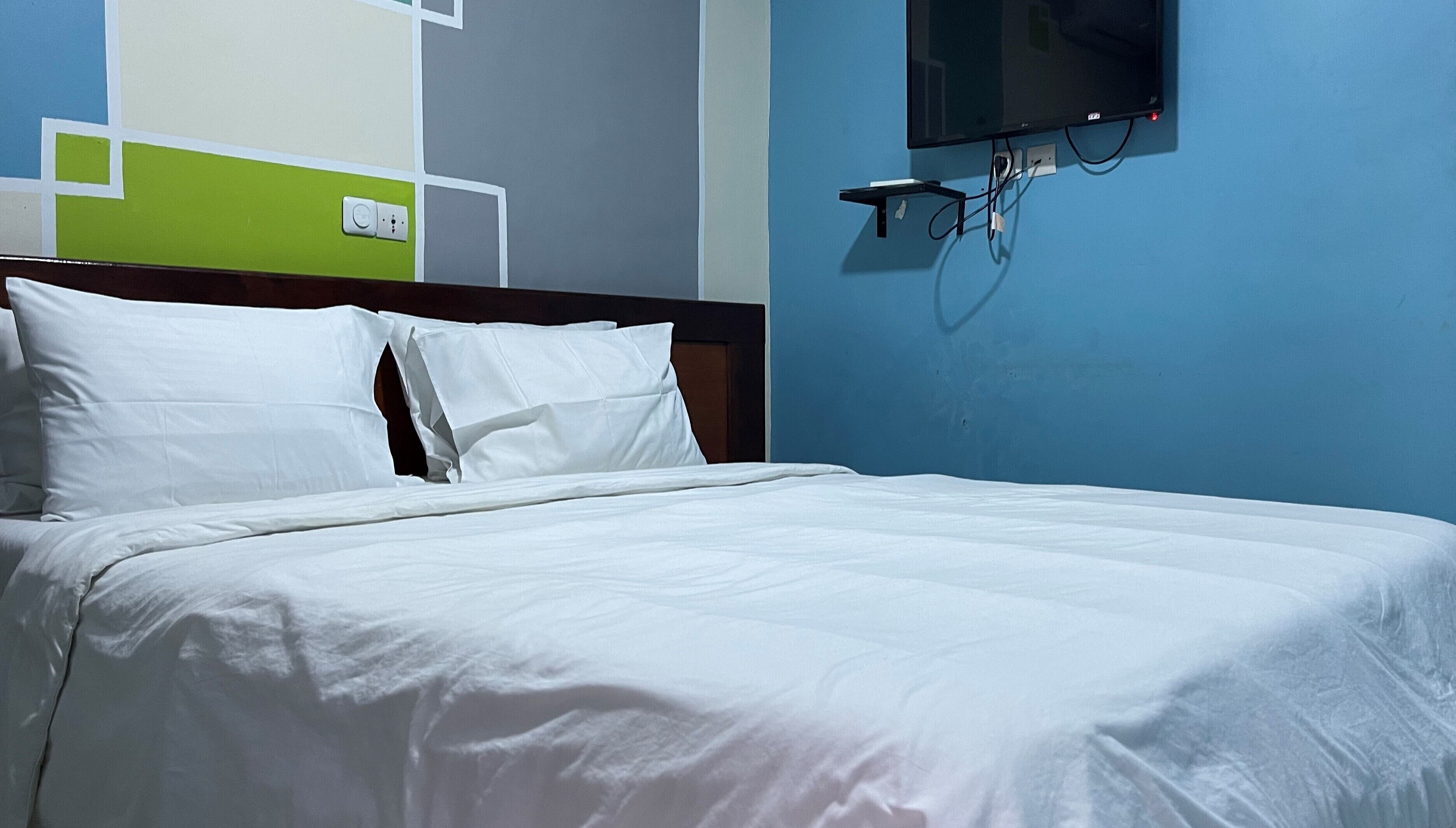 A neatly made bed with white linens in a room with a blue wall and a green accent wall.