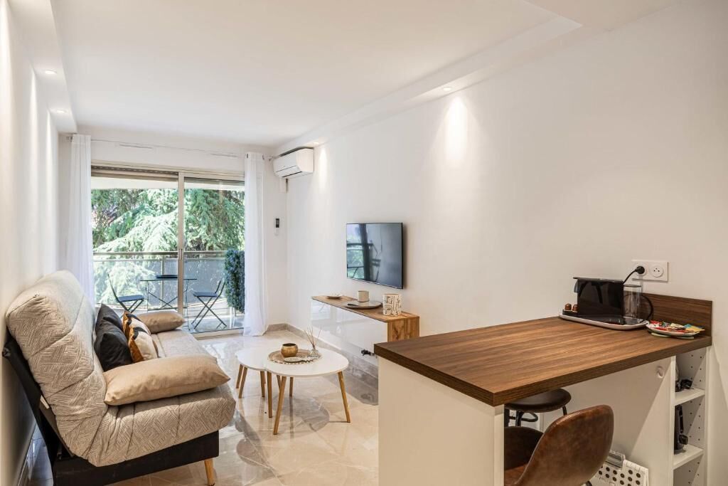 Un soggiorno moderno con un divano, un tavolino e una televisione. È presente un balcone con mobili da esterno.