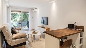 A modern living room with a sofa, a coffee table, and a TV. There is a balcony with outdoor furniture. - Le Center avec joli balcon et parking (Cannes)
