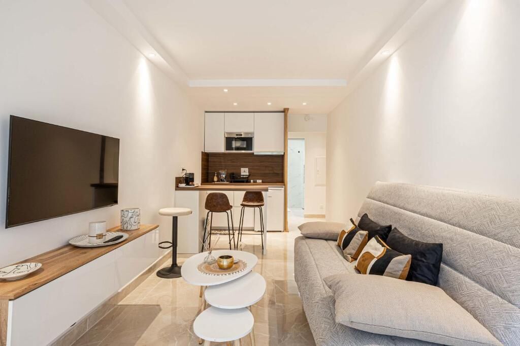 Un soggiorno moderno con un divano, una TV a parete e un angolo cottura sullo sfondo.