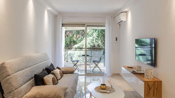 A modern living room with a sofa, a coffee table, and a TV mounted on the wall. - Le Center avec joli balcon et parking (Cannes)