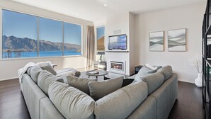 A modern living room with a large window offering a mountain view, a fireplace, and a comfortable seating area. - Luxury Retreat - Matakauri (Queenstown)