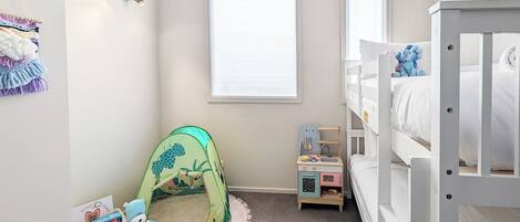 Een kinderkamer met stapelbedden, een box en een speelgoedkist.