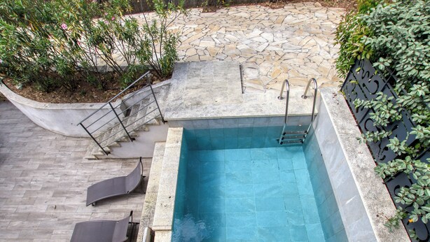 Une piscine rectangulaire entourée d’une terrasse en pierre, dotée de rampes et de marches en métal qui permettent d’y accéder.