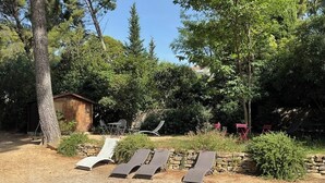 Un jardin avec un chalet en bois, un mur de pierres et trois chaises longues.