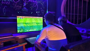 Two people playing a video game at a bar with neon lights and a large screen. - MBAR HOSTEL HAAD RIN  (Ko Pha-ngan)