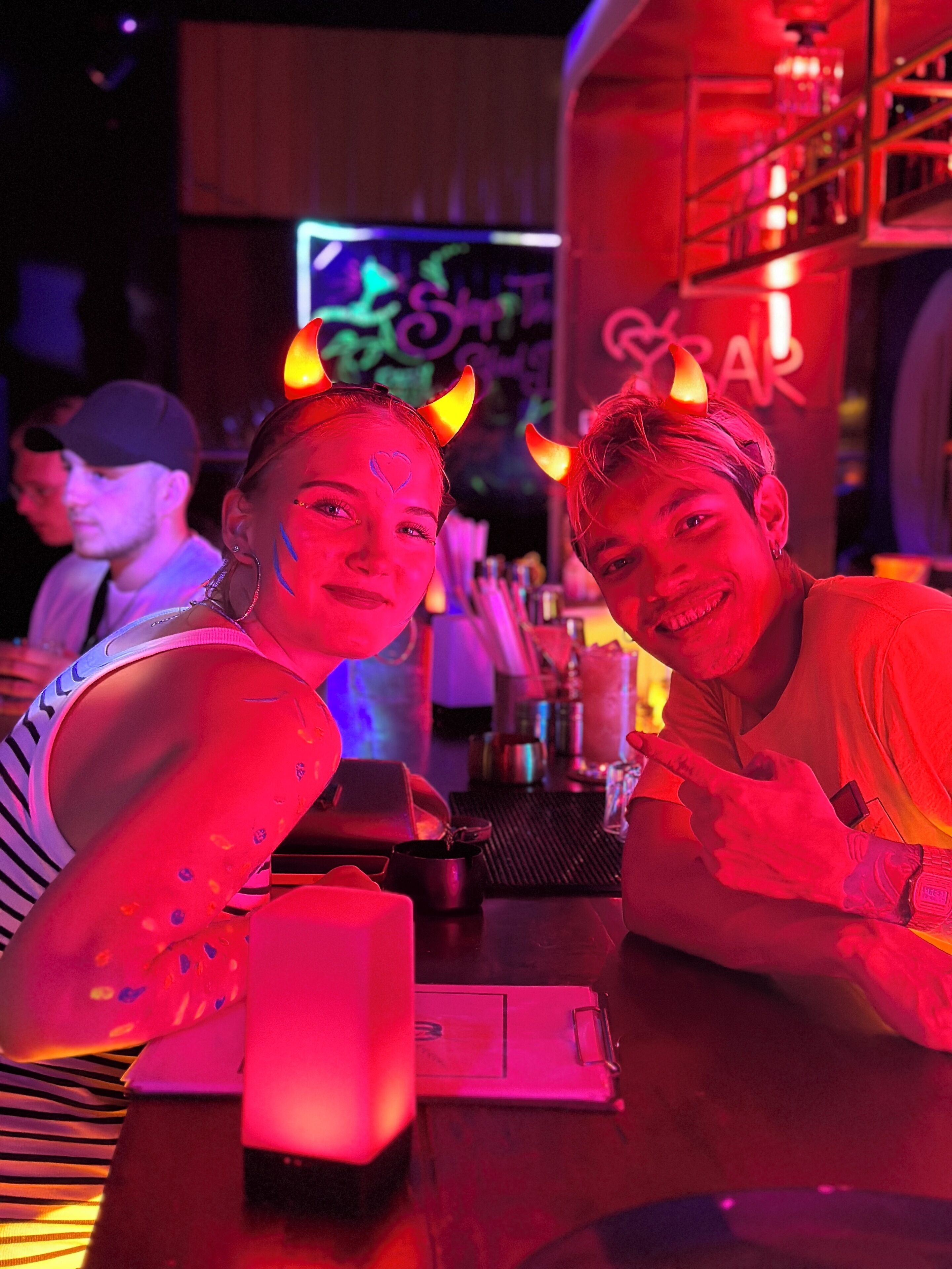 Two people at a bar with a neon sign in the background.