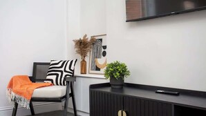 A modern living room with a sofa, a black and white patterned pillow, a potted plant, a remote control, and a framed artwork on the wall.