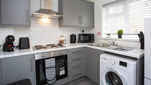A compact kitchen with grey cabinets, a microwave, a coffee maker, a dishwasher, and a washing machine.