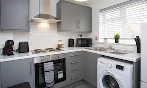 A compact kitchen with grey cabinets, a microwave, a coffee maker, a dishwasher, and a washing machine.