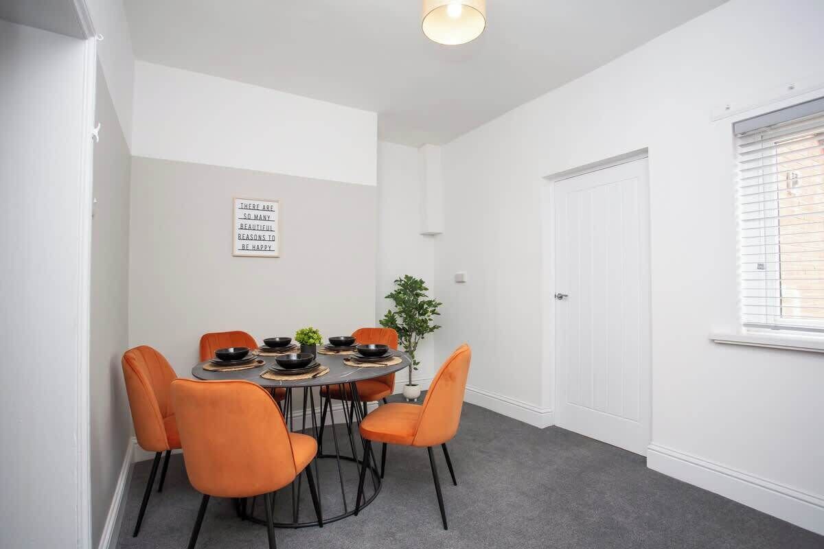 Un área de comedor con una mesa redonda, seis sillas color naranja y una planta en maceta.