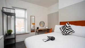 A hotel room with a bed, a desk, a chair, a mirror, and a radiator.