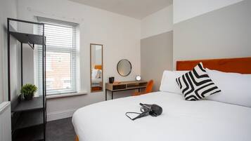 A hotel room with a bed, a desk, a chair, a mirror, and a radiator.