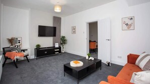 A modern living room with a flat-screen TV, a black console table, an orange sofa, and a grey carpet.