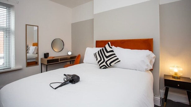 Een hotelkamer met een bed, een bureau met lamp, een spiegel en een raam met zonwering.