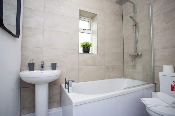 A bathroom with a white sink, a glass-enclosed shower, and a small window with a plant.