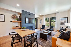 A modern living room with a fireplace, a dining area, and a sofa with cushions. - Virolet | Includes Two 1-Day Lift Tickets (Tamarack)