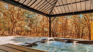 A hot tub area with a wooden deck and a covered roof, surrounded by trees. - The Firefly – A-Frame Cabin with Hot Tub, Arcade & 3 Living Rooms (Albrightsville)