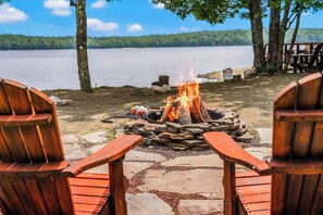 Un espace aménagé au bord du lac, avec un foyer et deux fauteuils Adirondack en bois placés face au feu.