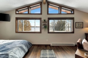 A bedroom with a bed, a wooden floor, a window, a wall-mounted TV, and a radiator.