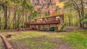 A cabin with a balcony, outdoor seating, and a covered patio area surrounded by trees.