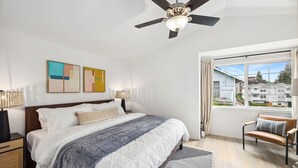 A bedroom with a bed, a ceiling fan, a window with curtains, and artwork on the wall. - Green Lake Remodelled home with AC, garage, yard (Seattle)