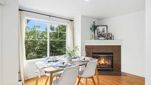 A dining room with a fireplace, a table set for four, and a view of greenery outside. - Green Lake Remodelled home with AC, garage, yard (Seattle)