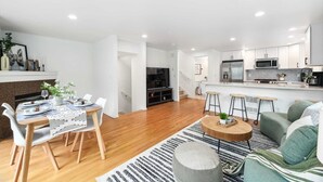 A modern living room with a dining area, a kitchen, and a staircase leading to an upper floor. - Green Lake Remodelled home with AC, garage, yard (Seattle)