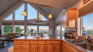A spacious kitchen with a large island, wooden cabinets, and a view of the outdoors. - Feathers + Fireweed (Homer)