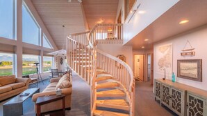 A spacious living area with a wooden spiral staircase, large windows offering a view of the outdoors, and a cozy seating arrangement. - Feathers + Fireweed (Homer)